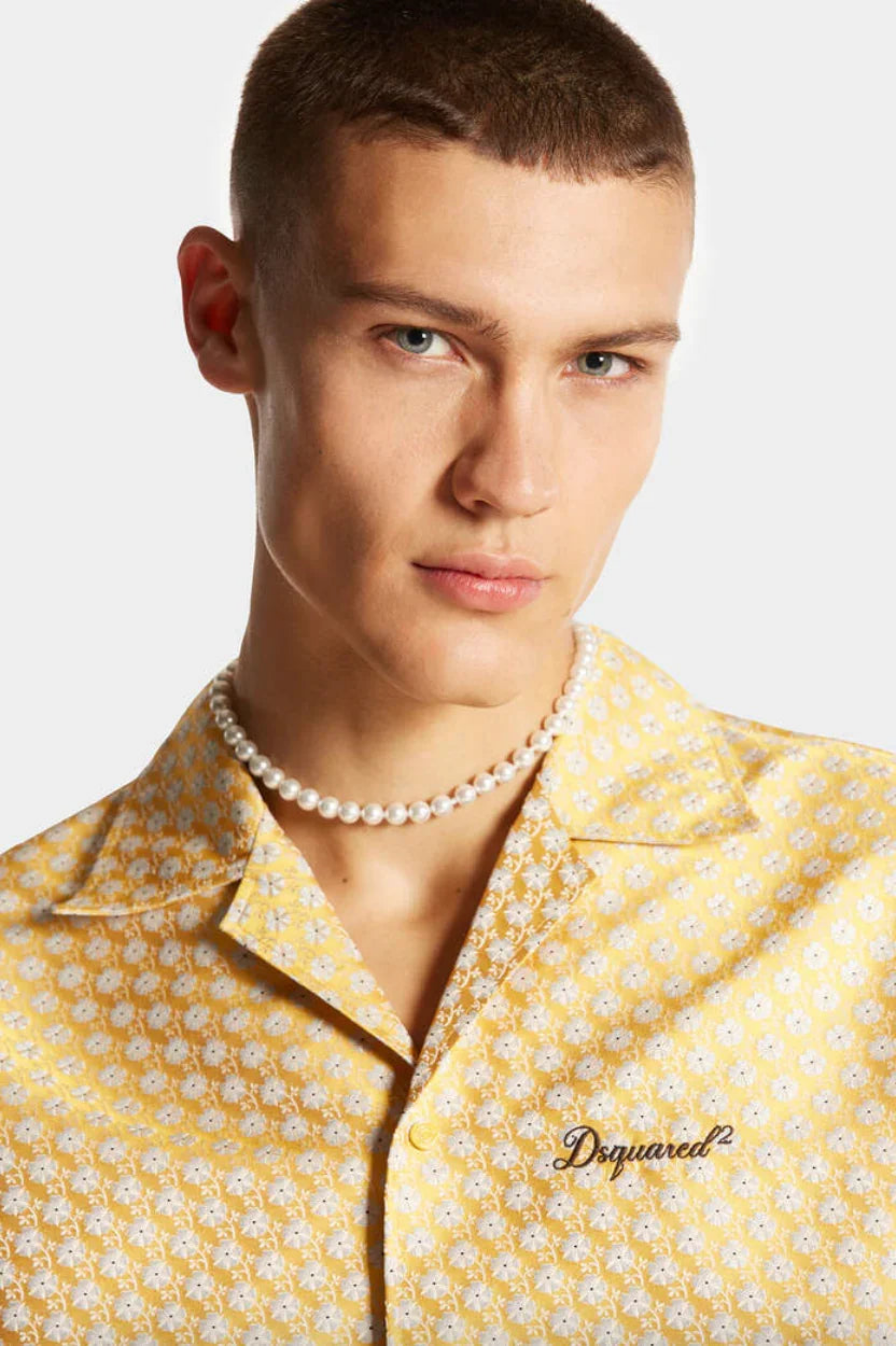 Close-up of man with short hair wearing a pearl necklace and yellow floral Dsquared2 shirt