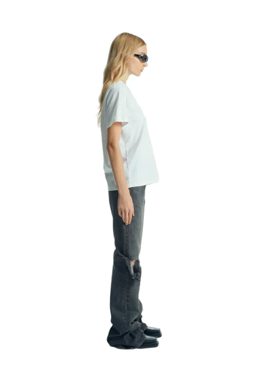 Side view of woman in white t-shirt, distressed black jeans, black square toe shoes, and black sunglasses