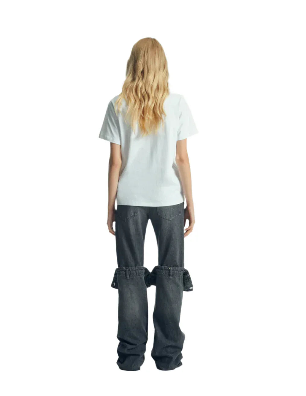 Rear view of woman with long blonde wavy hair wearing white t-shirt and black jeans with detachable lower legs