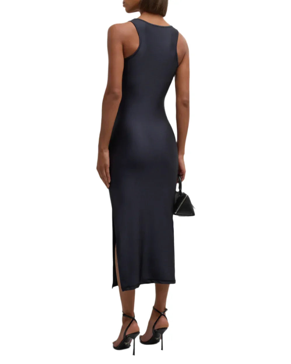 Back view of a woman wearing a black sleeveless midi dress with side slit, black heels, and holding a small black handbag