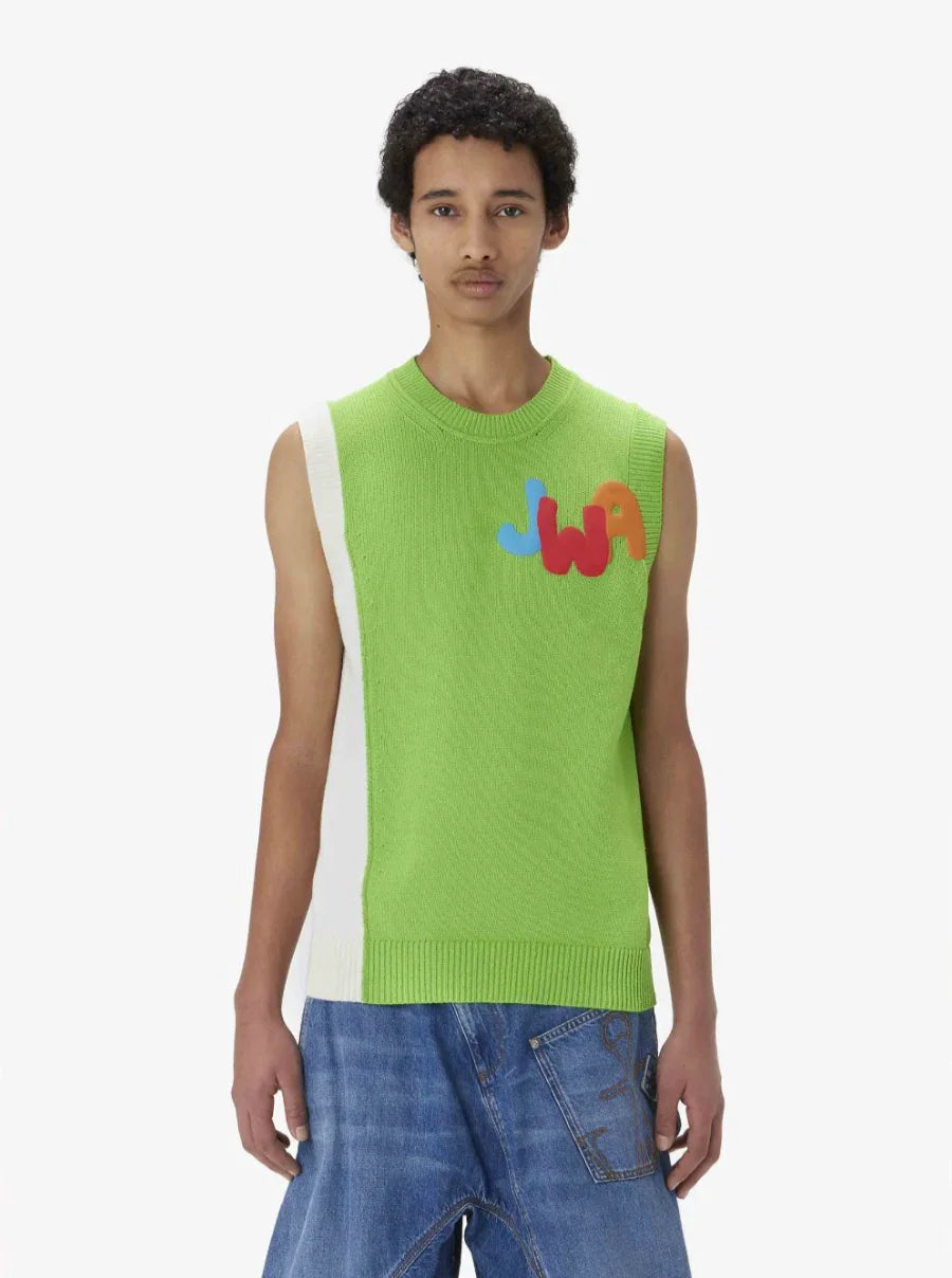 Man wearing sleeveless green and white knit sweater with colorful JWA logo and blue denim jeans