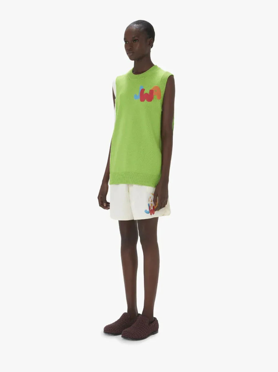 Model wearing lime green sleeveless sweater with multicolor logo and white shorts with matching logo
