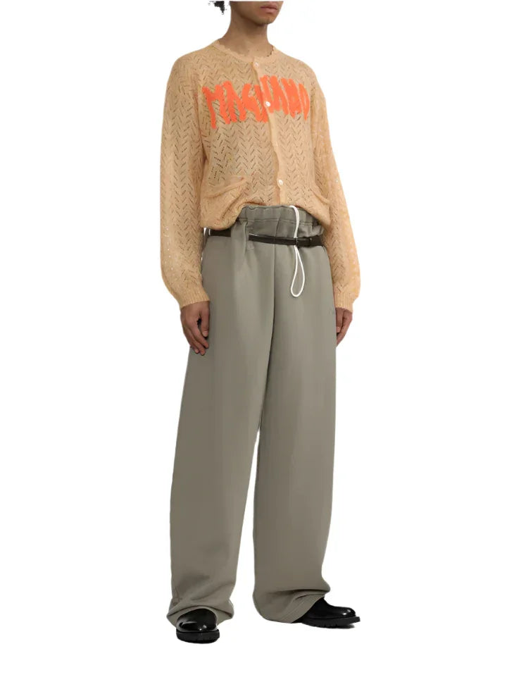 Model wearing beige knit cardigan with orange.logo and loose light gray wide-leg pants with black shoes