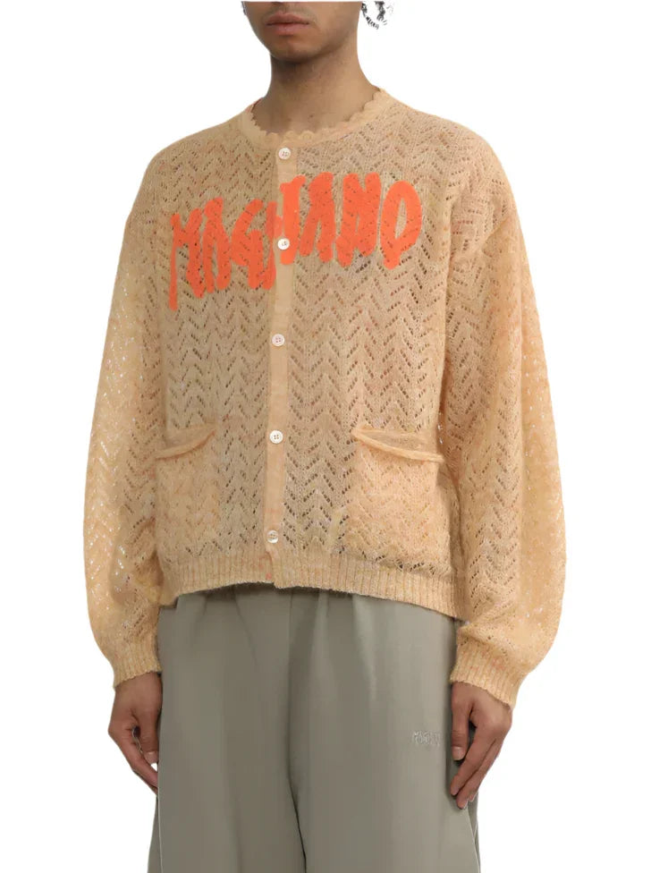 Beige open-knit cardigan with orange MOLLAKO knitwear logo and button front, worn with gray pants