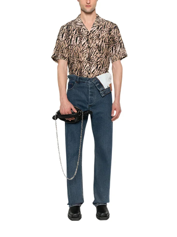 Man wearing animal print short-sleeve shirt, high-waisted blue jeans with visible white pocket, holding black handbag with silver chain