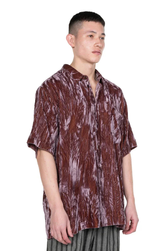 Man wearing a shiny textured brown short-sleeve button-up shirt with a collar and vertical striped pants