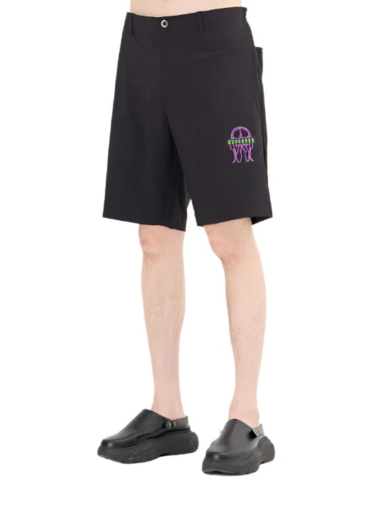Male model wearing black shorts with purple and green jellyfish embroidery and black slip-on shoes