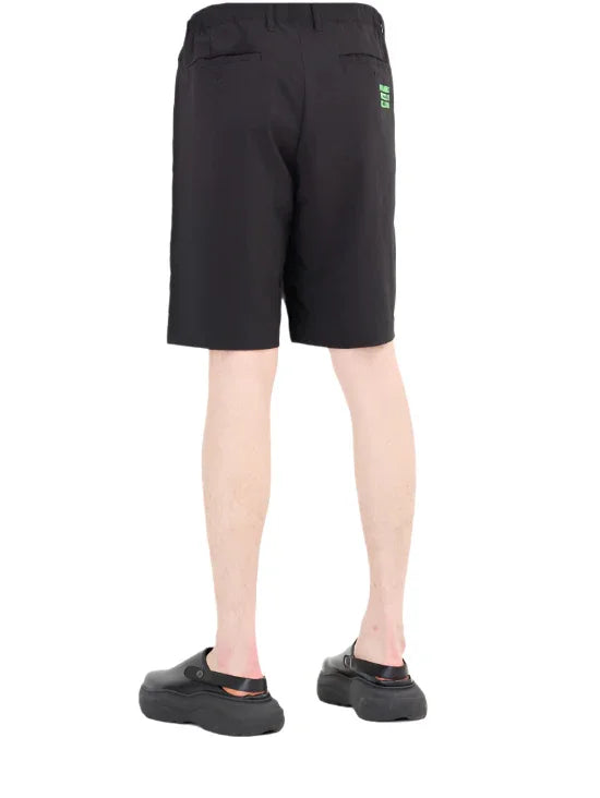 Man wearing black casual shorts and black slip-on shoes, shown from the back on white background