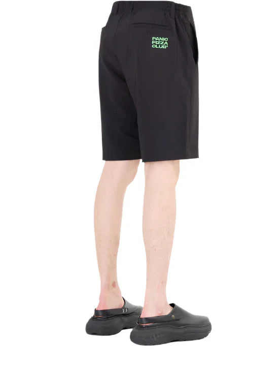 Rear view of a person wearing black shorts with green Panio Pizza Club logo and black slip-on shoes