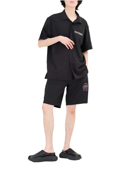 Man wearing black short-sleeve button-up shirt and matching shorts with colorful graphic details