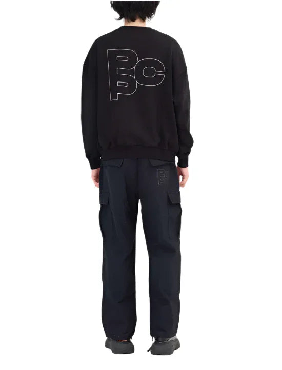 Person wearing black oversized sweatshirt and cargo pants with PCPP logo, standing back view