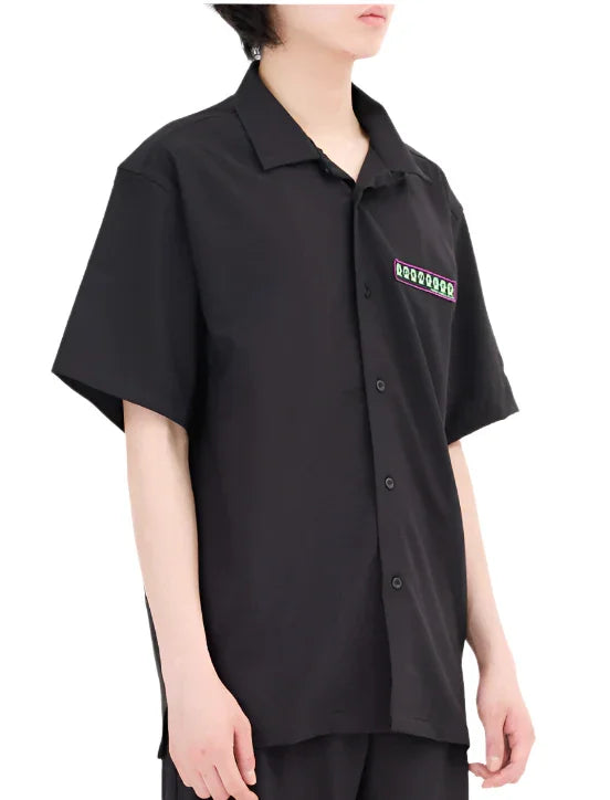 Person wearing black short-sleeve button-up shirt with colorful patch on left chest pocket