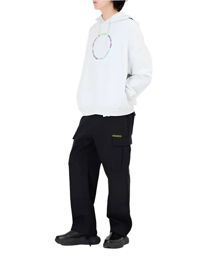 Person wearing white hoodie with circular green and purple text and black cargo pants with green logo pocket