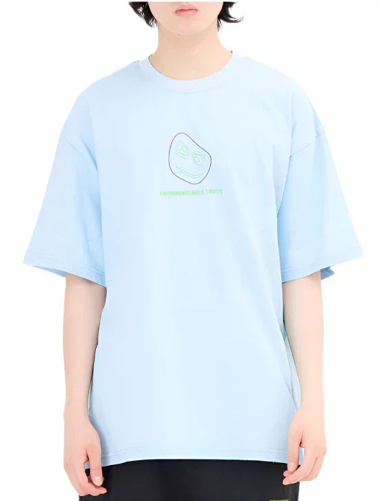 Person wearing light blue oversized T-shirt with simple abstract face graphic and green text