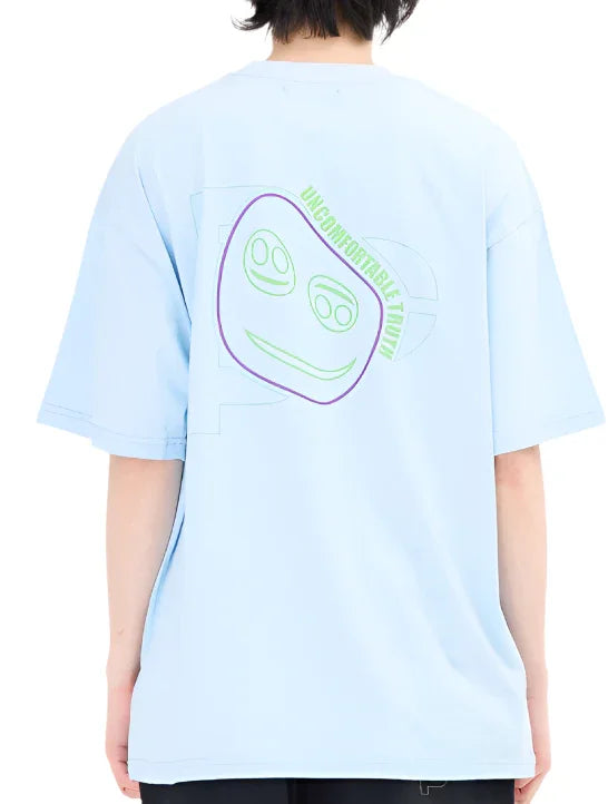 Person wearing light blue oversized T-shirt with green and purple abstract face and text 'Uncomfortable Truth' on back