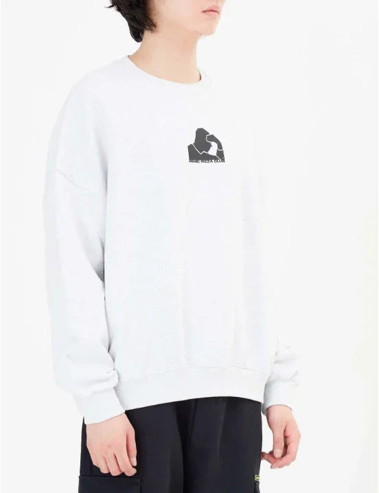 Person wearing white sweatshirt with small black graphic and black pants in studio setting