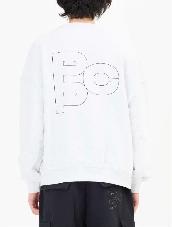 Person wearing white sweatshirt and black pants with large PCP logo on back and smaller logo on pants