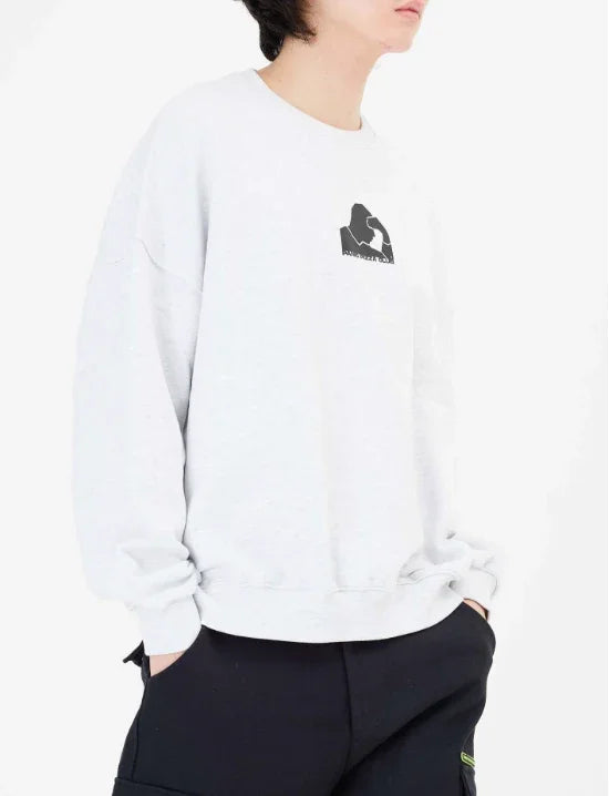 Person wearing white oversized sweatshirt with black graphic logo and black pants against white background