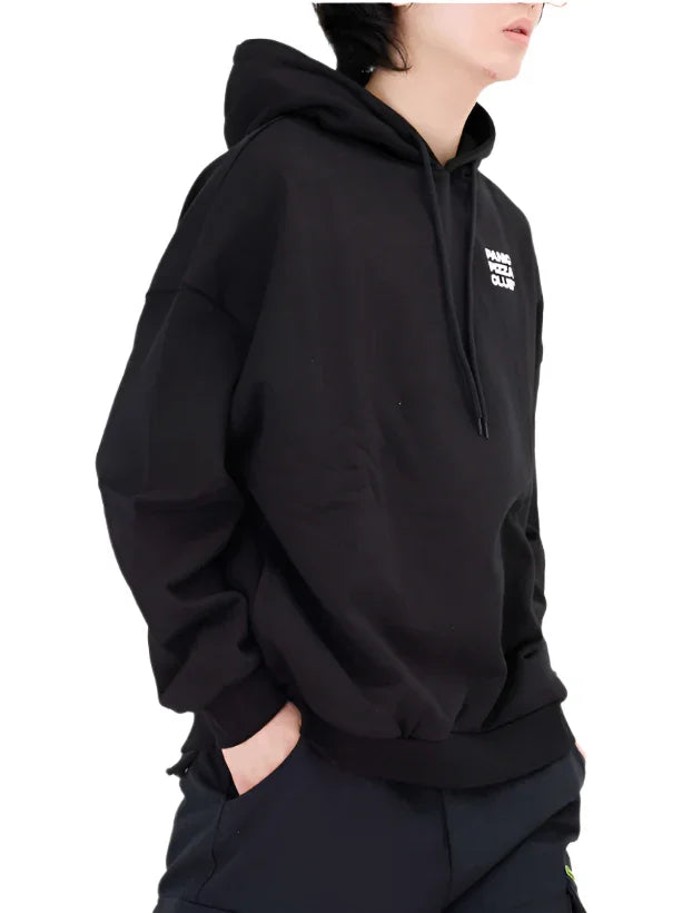 Person wearing black Paris Police Club hoodie with hands in pockets against white background