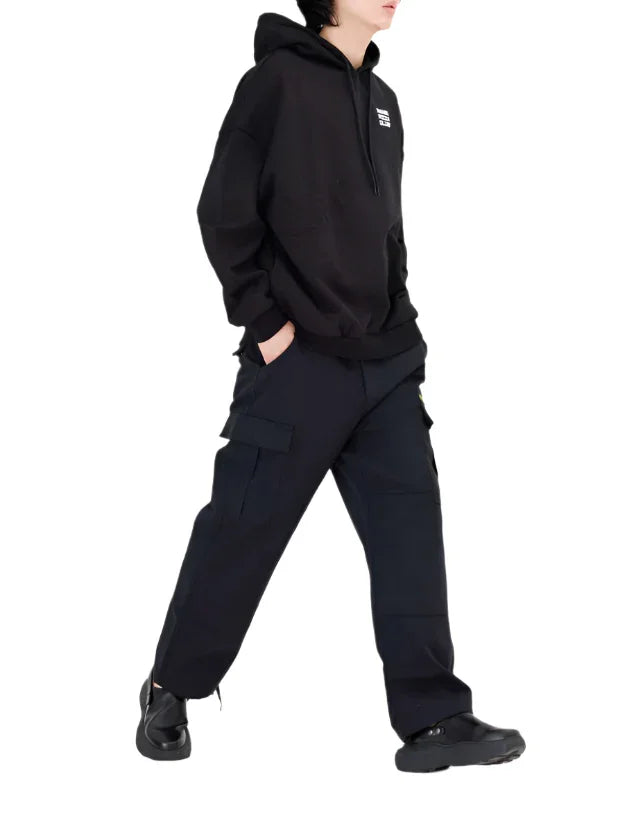 Person wearing black hoodie and cargo pants with hands in pockets walking against white background