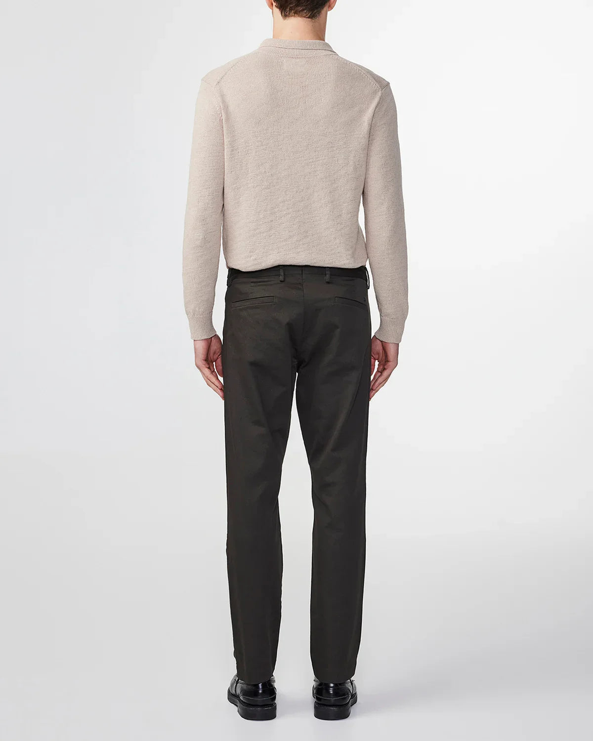 Male model wearing beige sweater and black tailored pants with black shoes, standing against white background