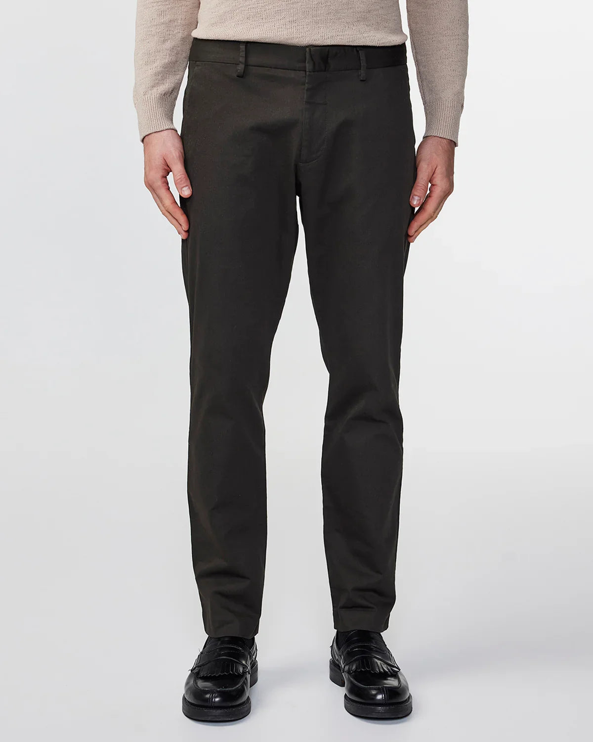 Man wearing dark green slim-fit pants, beige sweater, and black leather loafers on white background