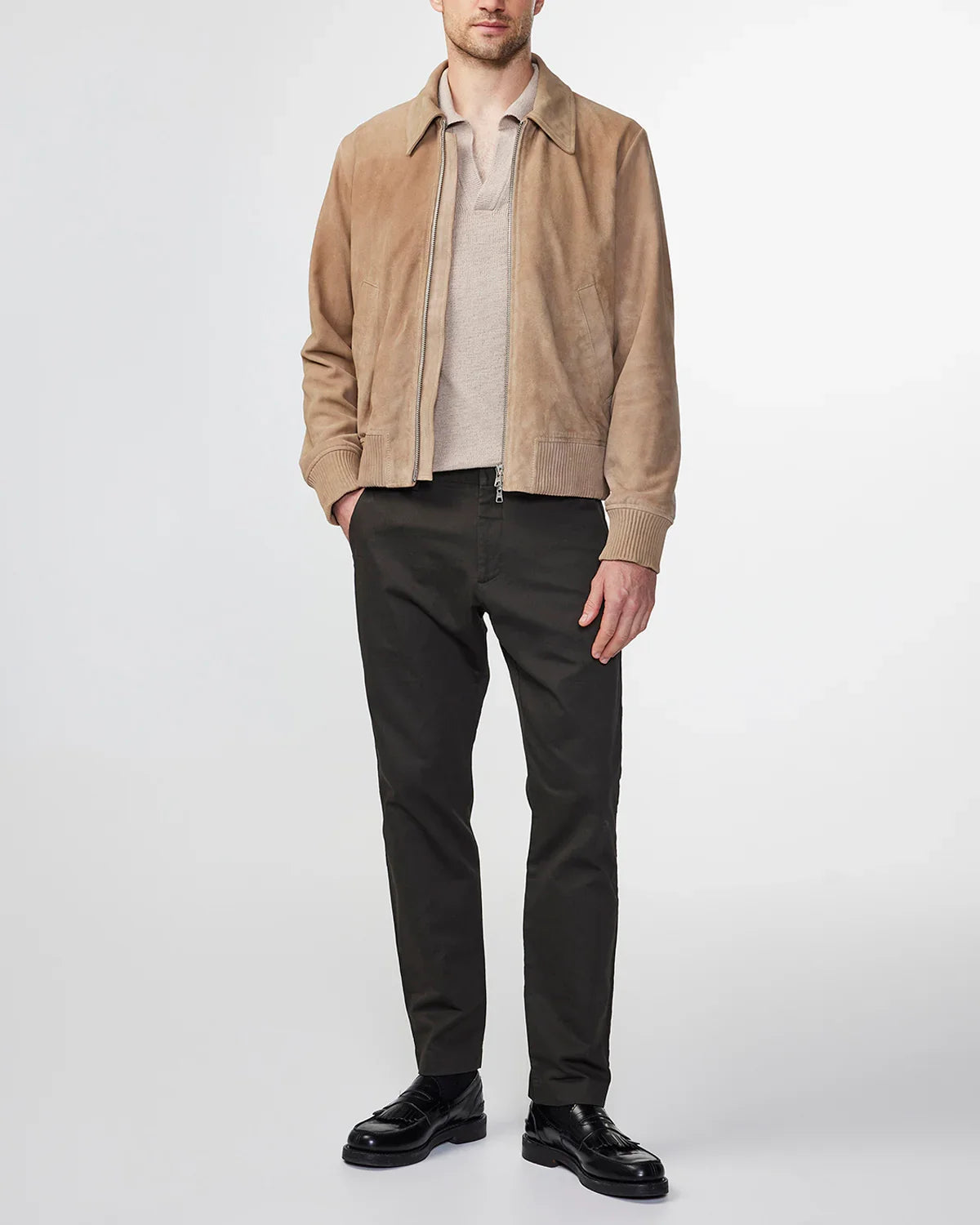 Man wearing beige suede jacket, light beige shirt, black pants, and black leather shoes on white background
