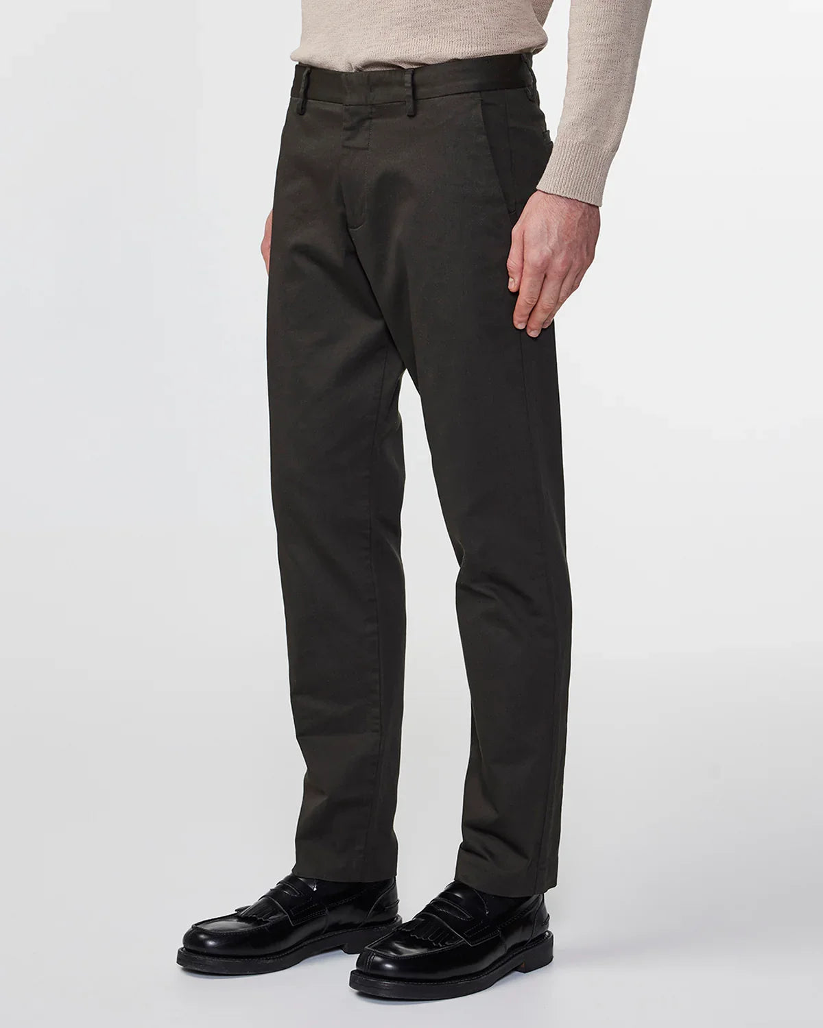 Men's dark brown tailored trousers paired with black leather loafers and beige knit sweater sleeve