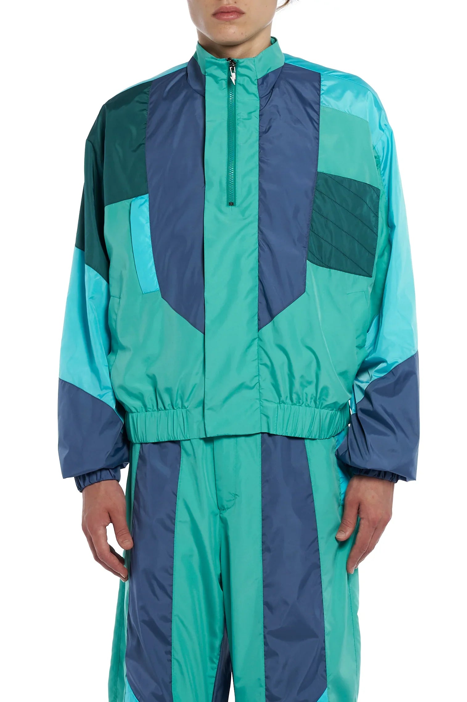 Man wearing a teal and navy blue color-block tracksuit jacket and matching pants