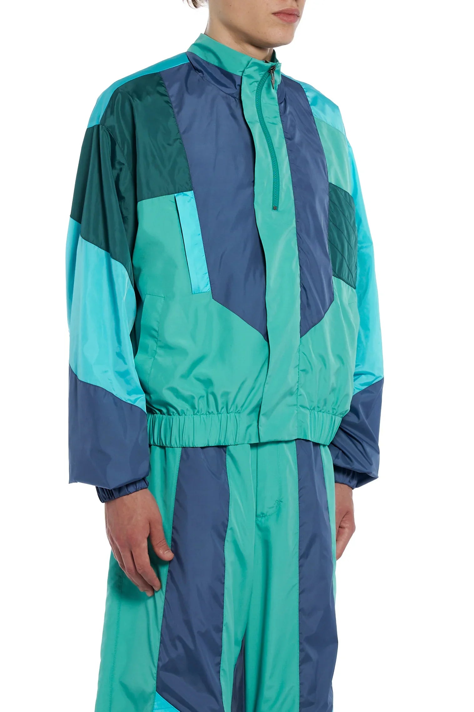 Male model wearing a teal and navy blue color-block nylon tracksuit jacket and matching pants