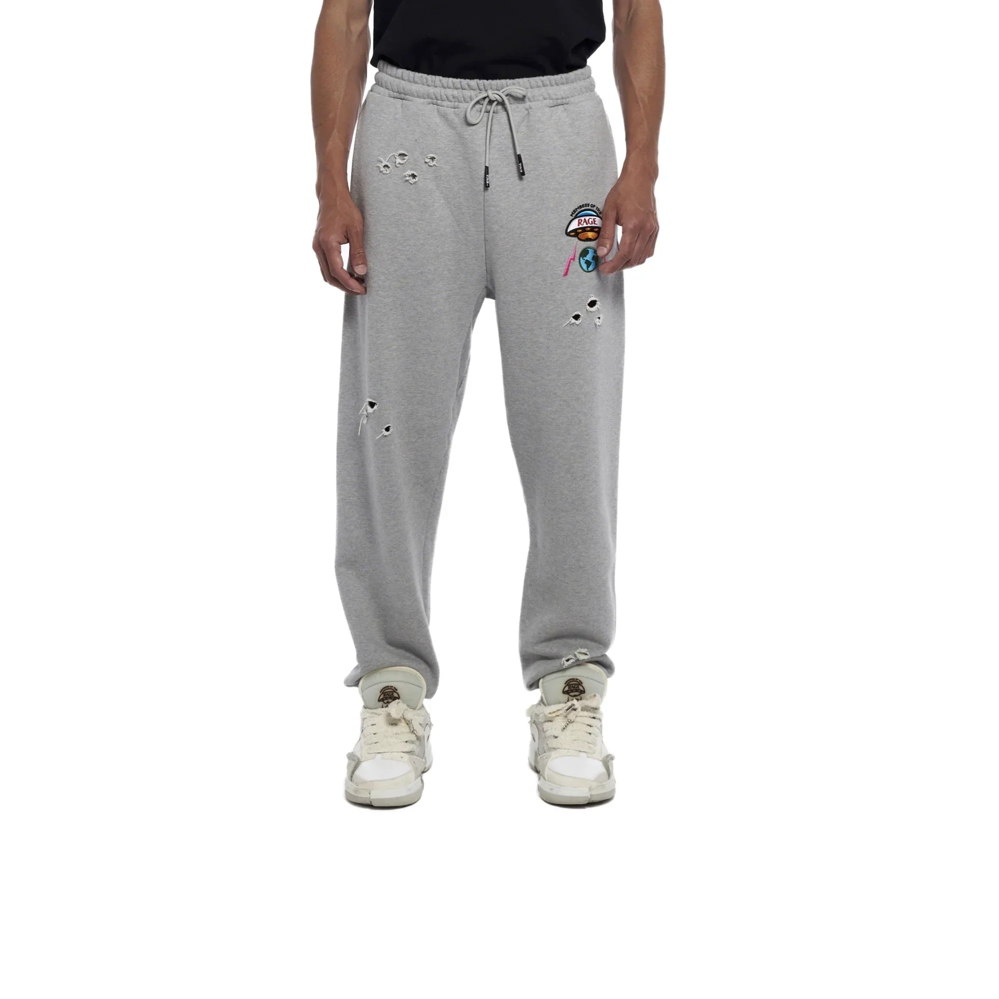 Man wearing grey distressed sweatpants with colorful patch and white sneakers on white background