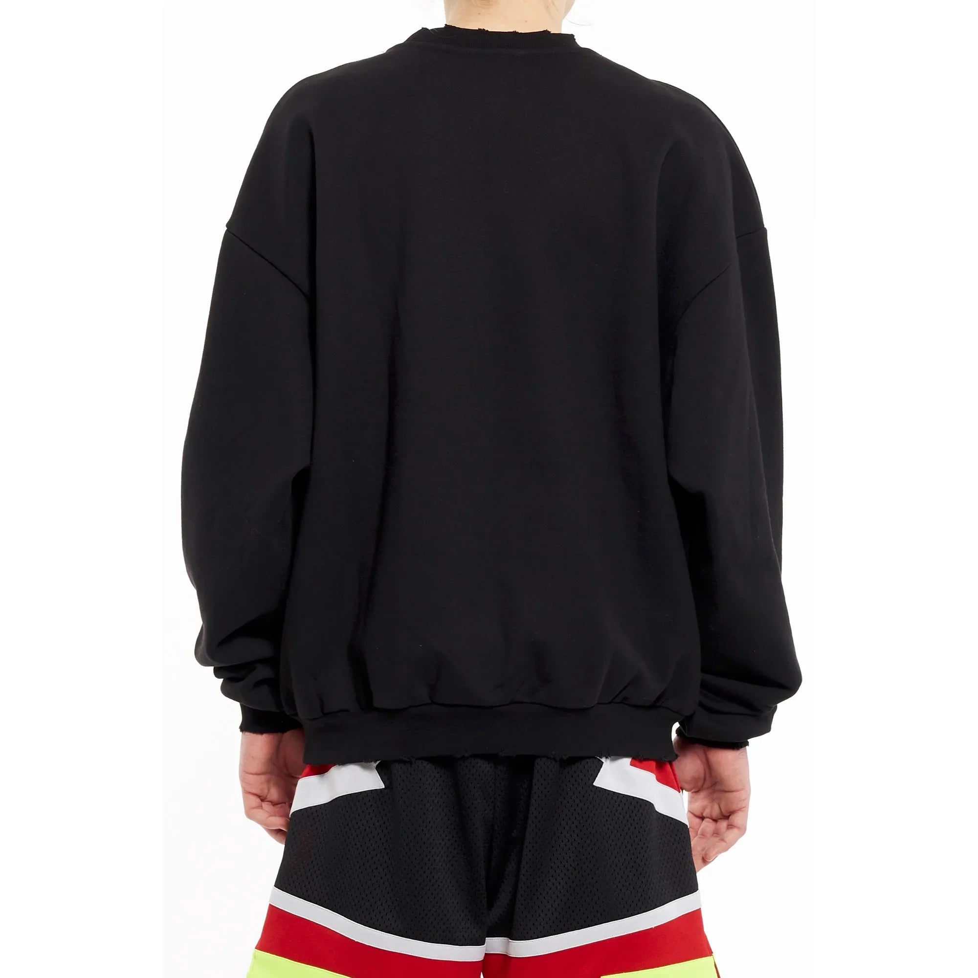 Back view of person wearing black oversized sweatshirt and colorful mesh shorts with red, white, and yellow accents