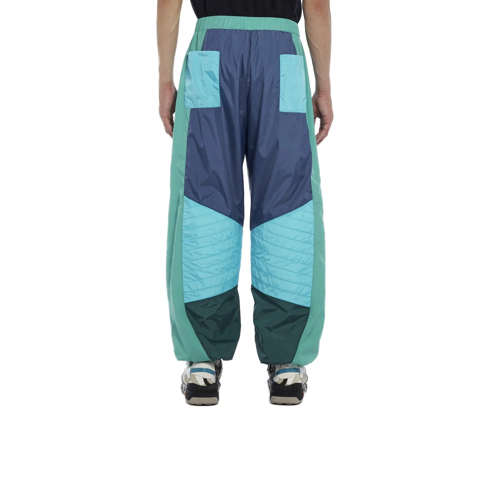 Back view of man's color-blocked pants in shades of teal, blue, and dark green with pockets and sneakers
