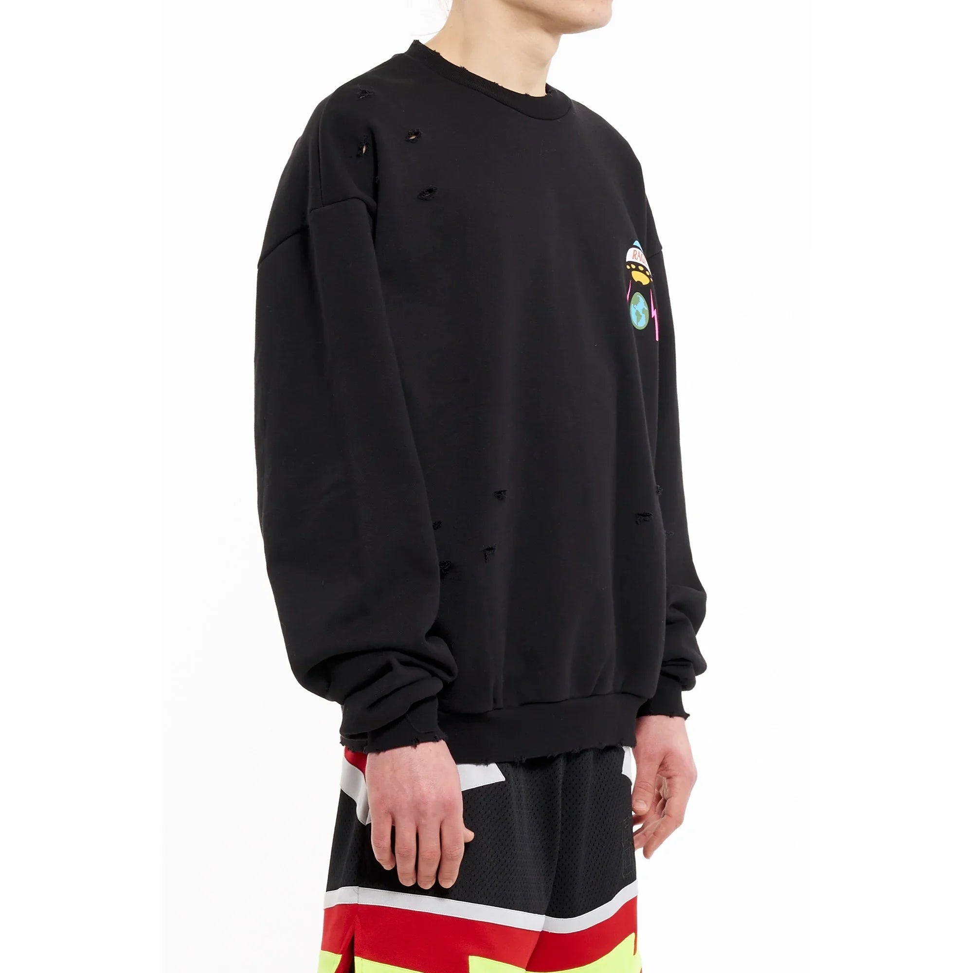 Side view of a person wearing a black distressed sweatshirt with colorful graphic and multicolor sports shorts