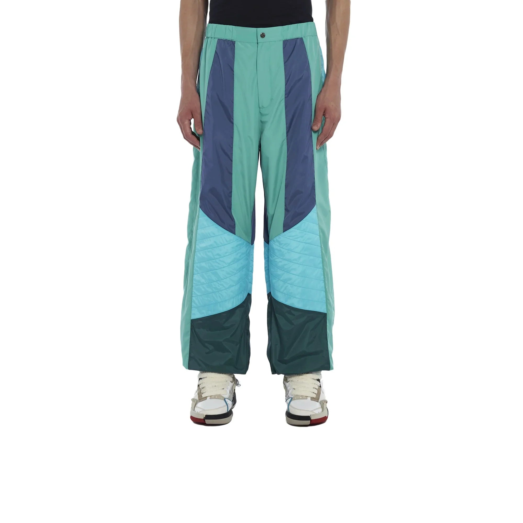 Men's colorblock winter pants with teal, navy, and light blue panels paired with white sneakers