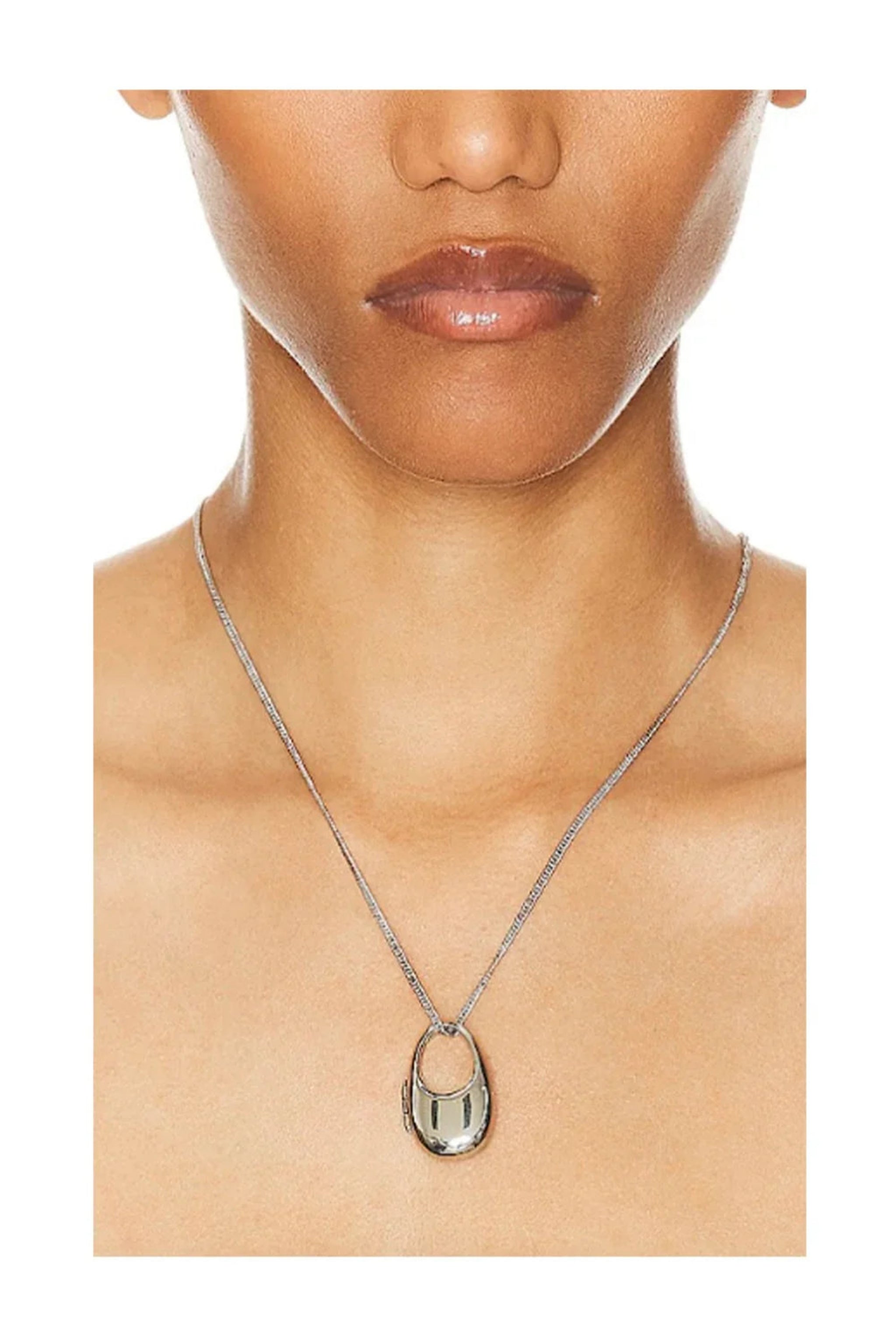 Close-up of woman wearing a sleek silver chain necklace with an oval silver pendant