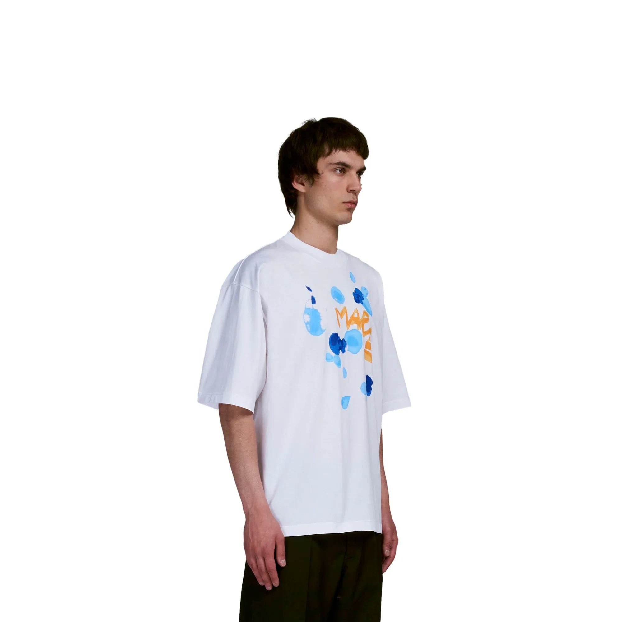 Young man wearing white oversized T-shirt with blue paint splatter and orange text graphic