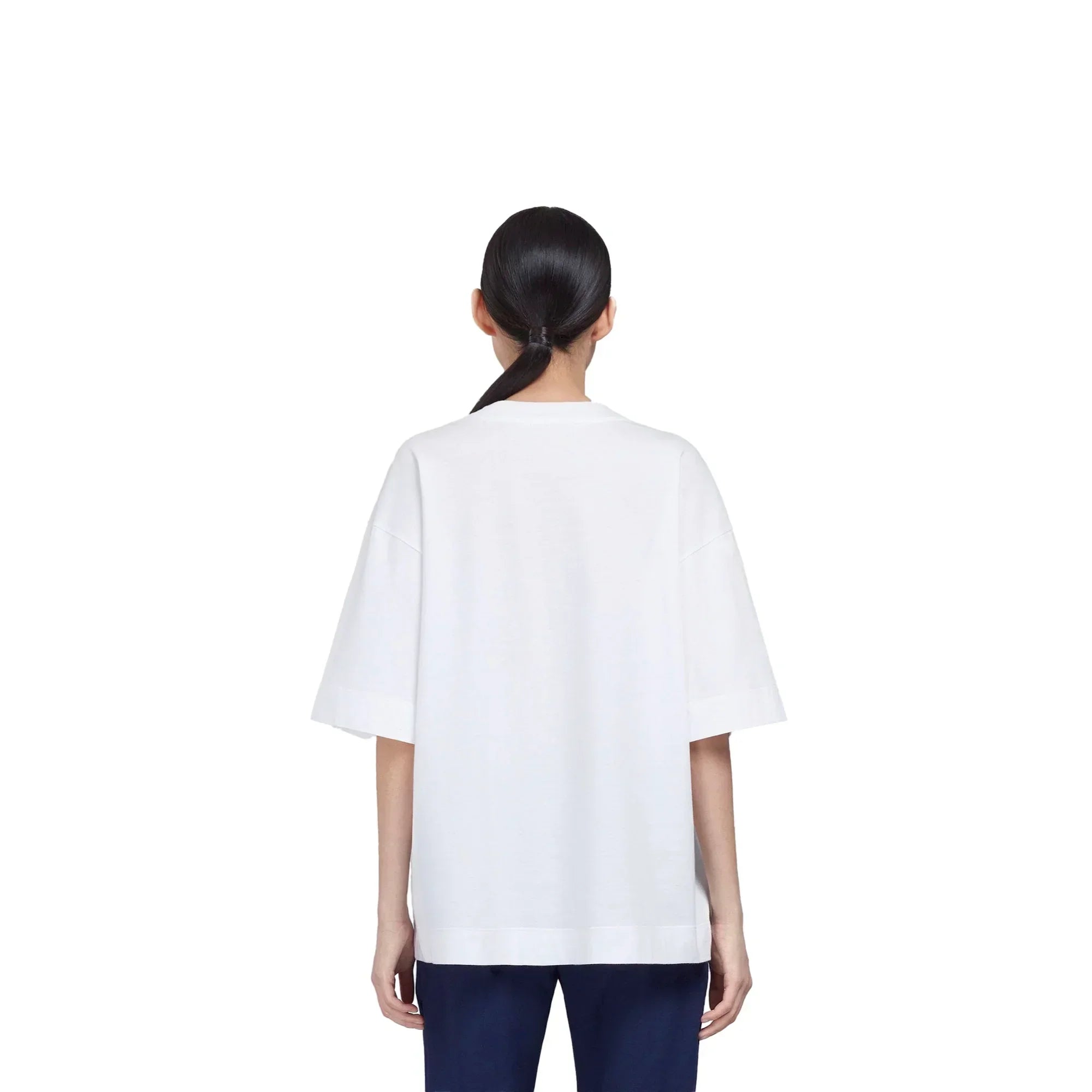 Woman with ponytail wearing plain white oversized T-shirt and navy pants, back view on white background