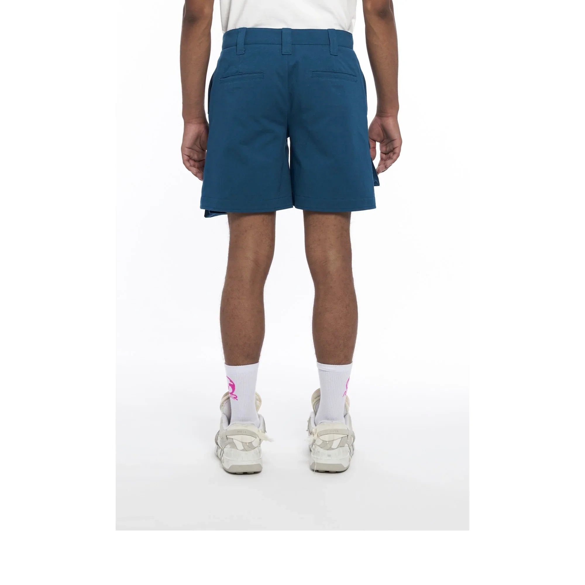 Rear view of person wearing blue casual shorts, white socks with pink logo, and white sneakers on white background