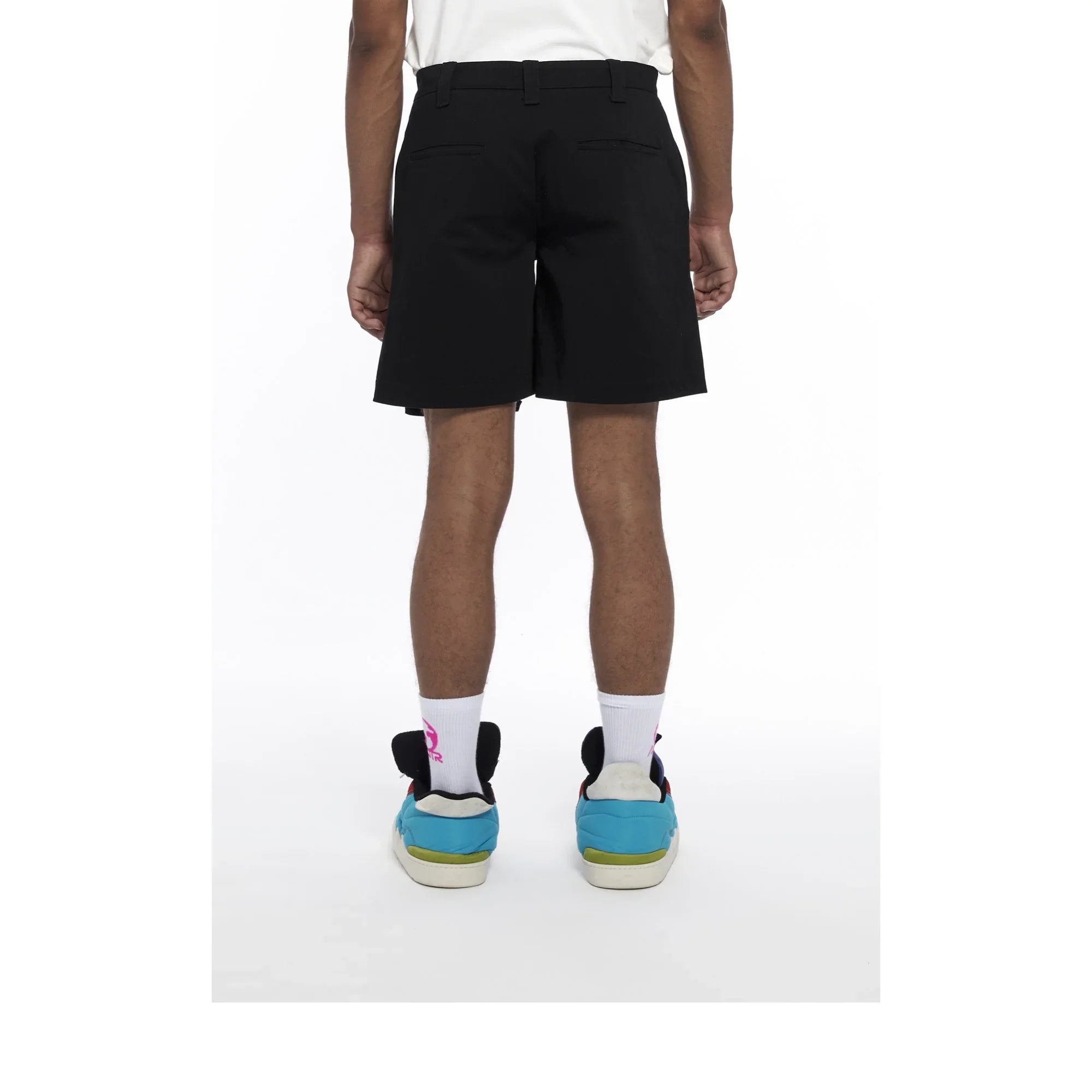 Rear view of a person wearing black casual shorts, white socks, and blue sneakers on white background