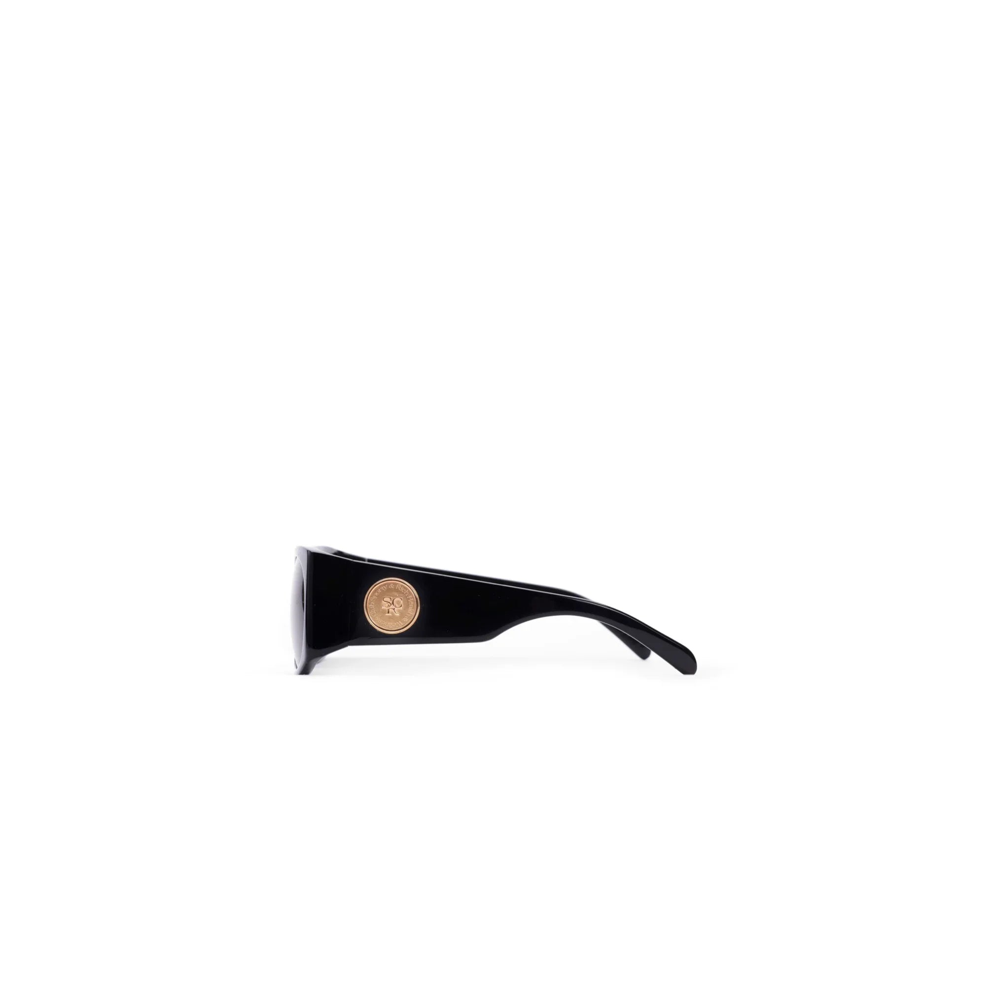 Side view of black sunglasses with thick arms and a gold circular logo badge