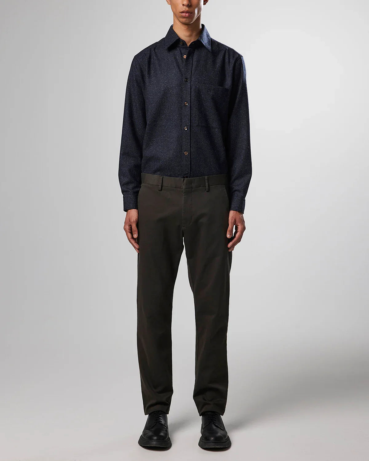 Man wearing navy blue button-up shirt, dark brown trousers, and black dress shoes on gray background